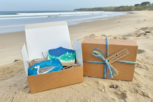 Load image into Gallery viewer, Coastal gift set with one blue colour felted soap with a seagull image needlefelted onto it and one seascape soap which depicts the beach and ocean waves.
They come in a gift box tied with blue & turquoise jute string. The picture has a beach background.