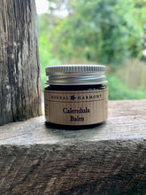 Load image into Gallery viewer, A 15ml glass jar with aluminium lid of Calendula Balm on wooden surface.