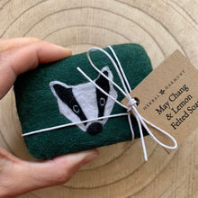 Load image into Gallery viewer, Green felted soap with badger design held by a hand, tied with hemp twine and a recycled paper tag, on a wooden surface. 
