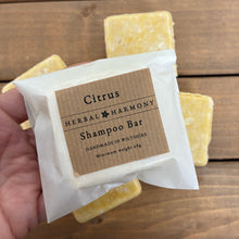 Load image into Gallery viewer, Handmade square shaped citrus shampoo bar by 'Herbal Harmony' on a wooden background. The bars are yellow coloured from yellow clay and packaged in an Eco friendly glassine paper bag. 
Natural, vegan and plastic free haircare. 
Citrus shampoo bar is scented with May Chang, orange and lime essential oils and the active ingredients include Panthenol, argan oil, jojoba oil, cocoa butter and coconut oil. 
