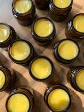 Load image into Gallery viewer, Lots of glass jars on a wooden surface containing calendula balm which is yellow coloured from the Beeswax &amp; Calendula extract used to make it.
